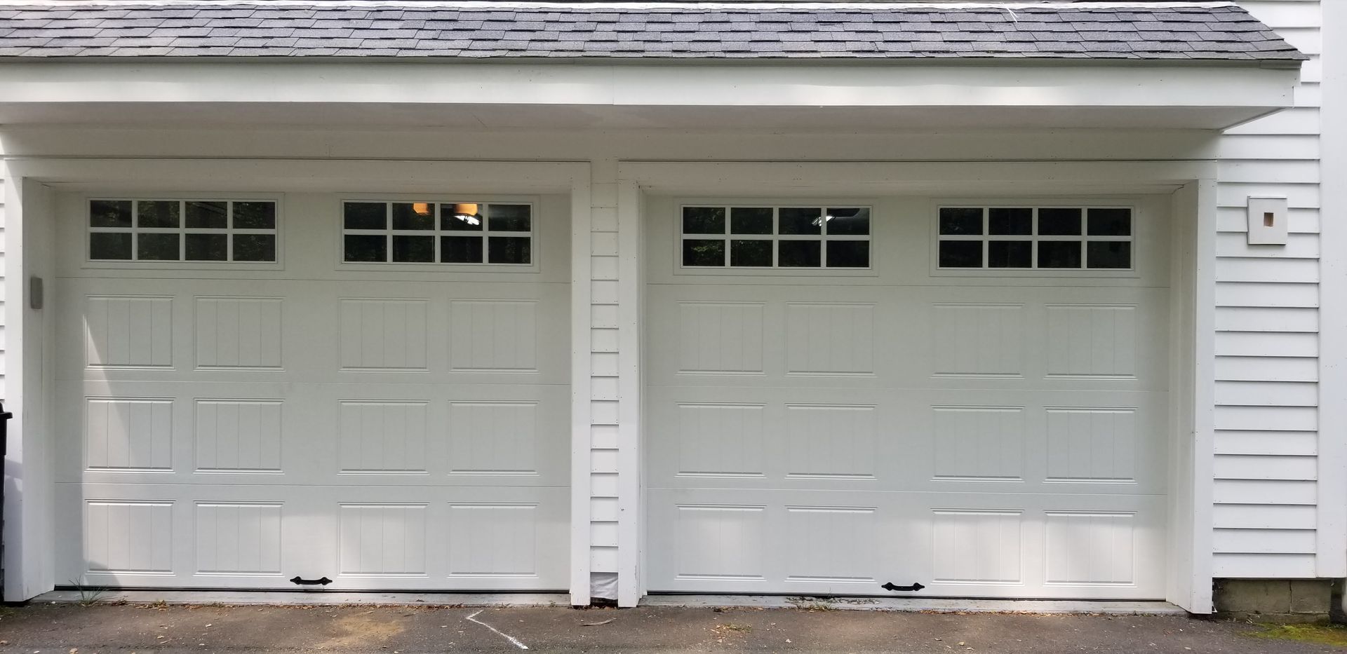 White double garage doors on a house exterior with small windows above each door.