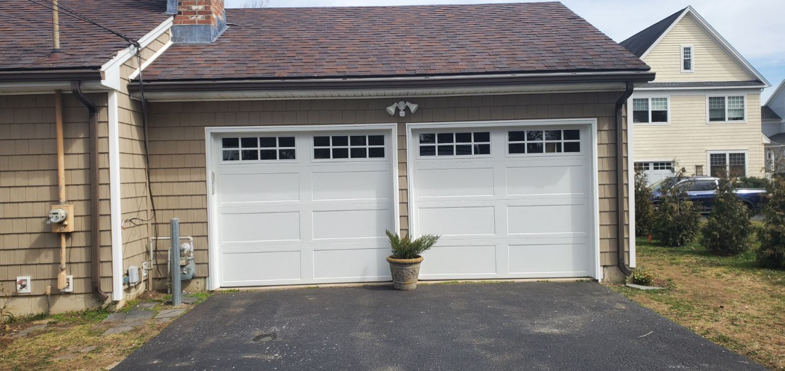 White double garage doors on a beige house with a small potted plant in front.