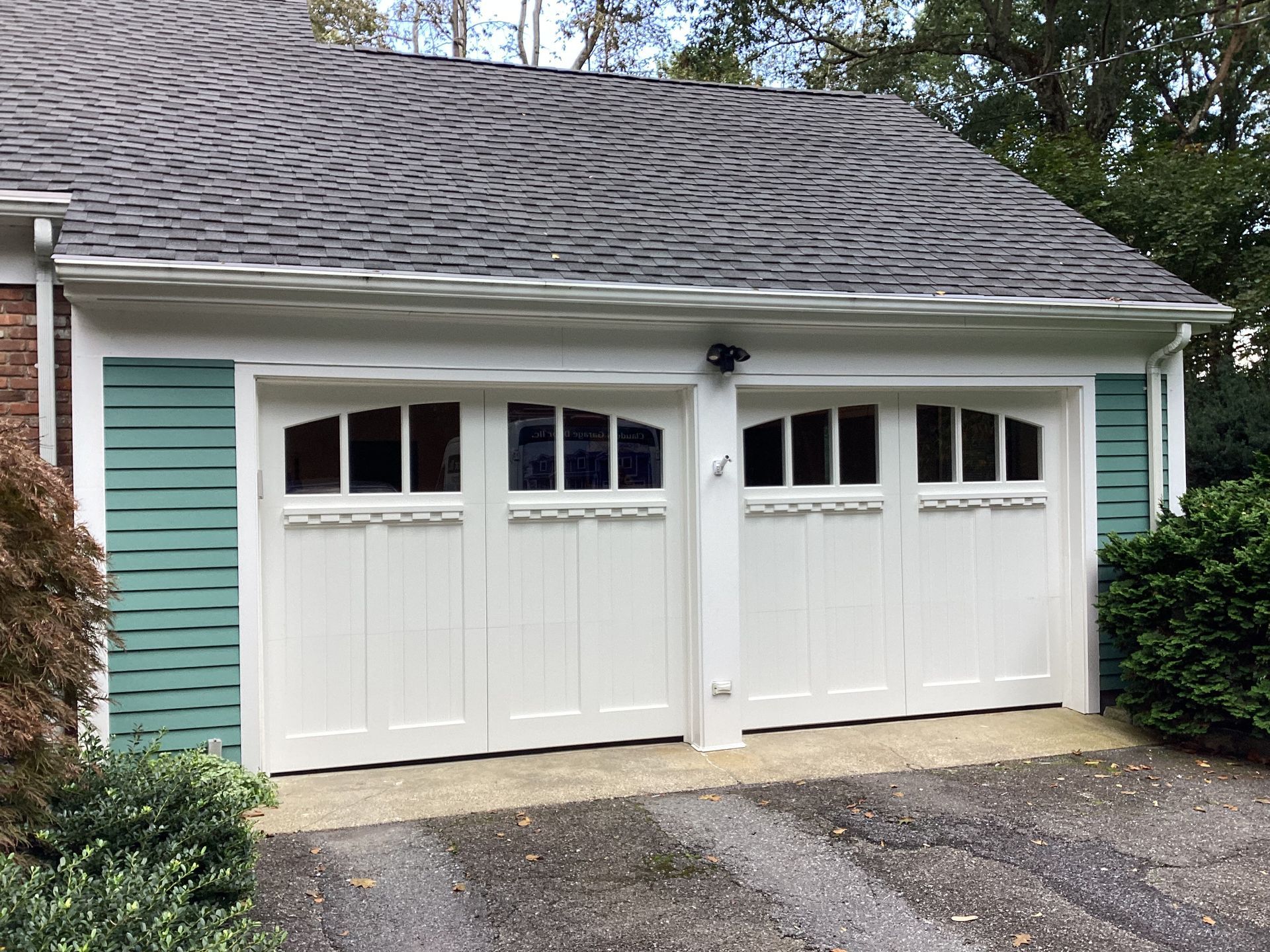 White double garage doors on a teal house with a shingled roof and driveway.