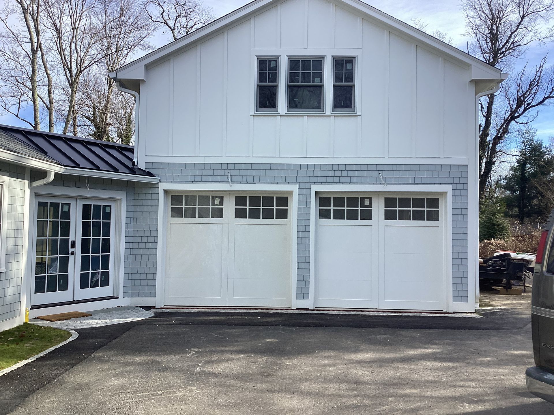 White two-story garage with two doors and a side entry, attached to a house under a clear sky.
