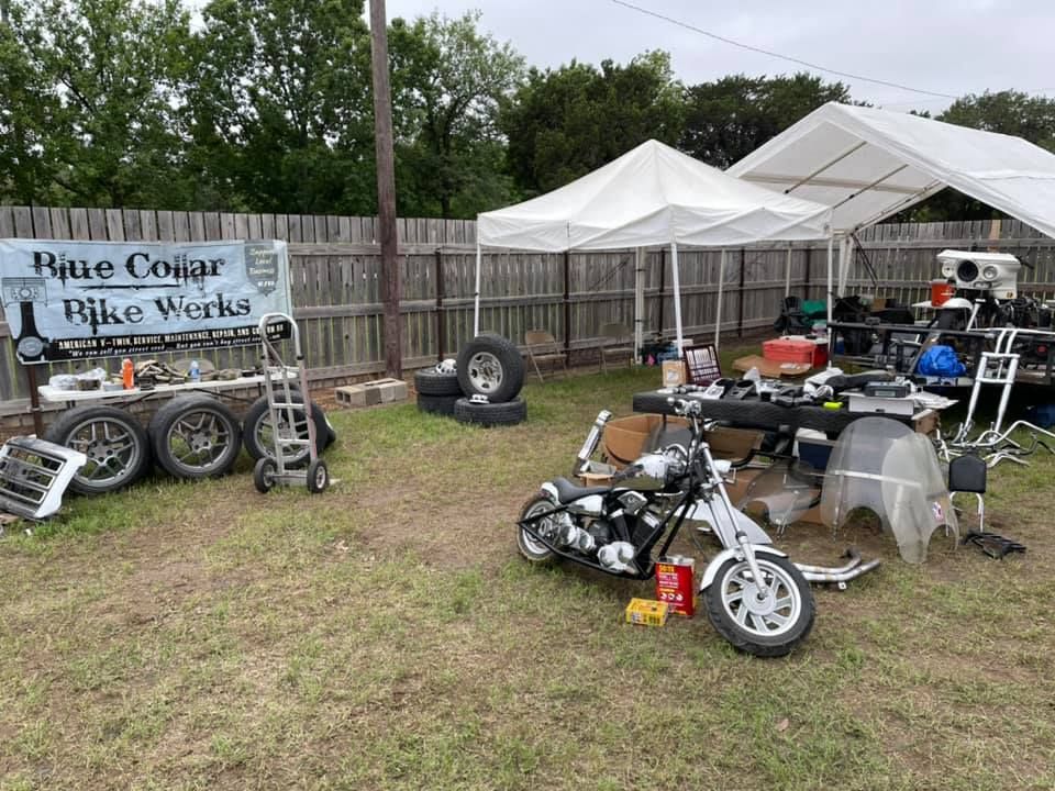Backyard motorcycle repair shop with parts and a motorcycle on display under a tent.