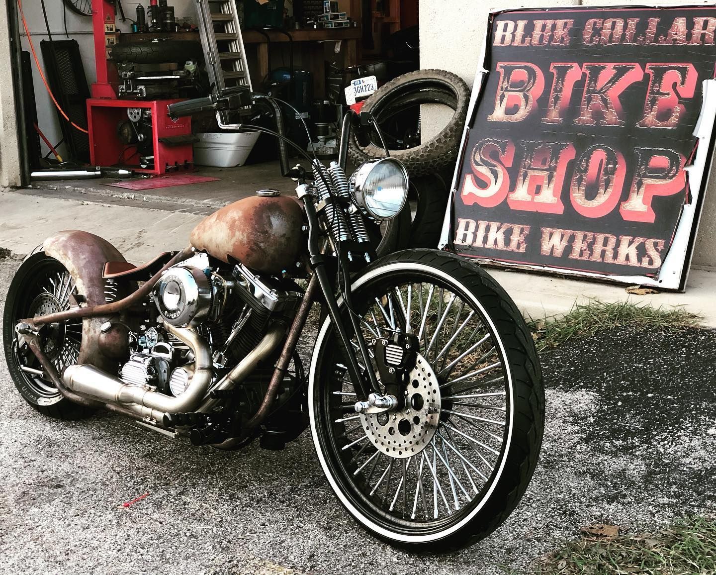 Rusty custom motorcycle parked in front of a bike shop sign.