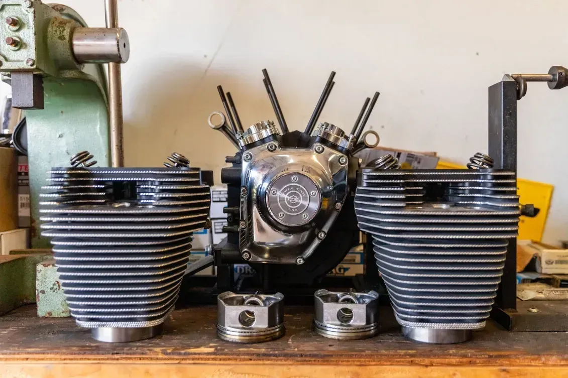 Motorcycle engine parts: cylinders, pistons, and a chrome-plated crankcase arranged on a workbench.