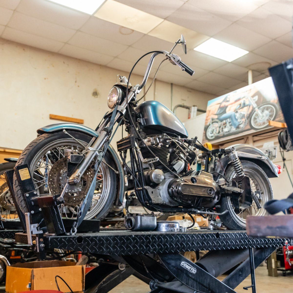 Motorcycle on a lift in a workshop with a light blue gas tank, ready for repair.
