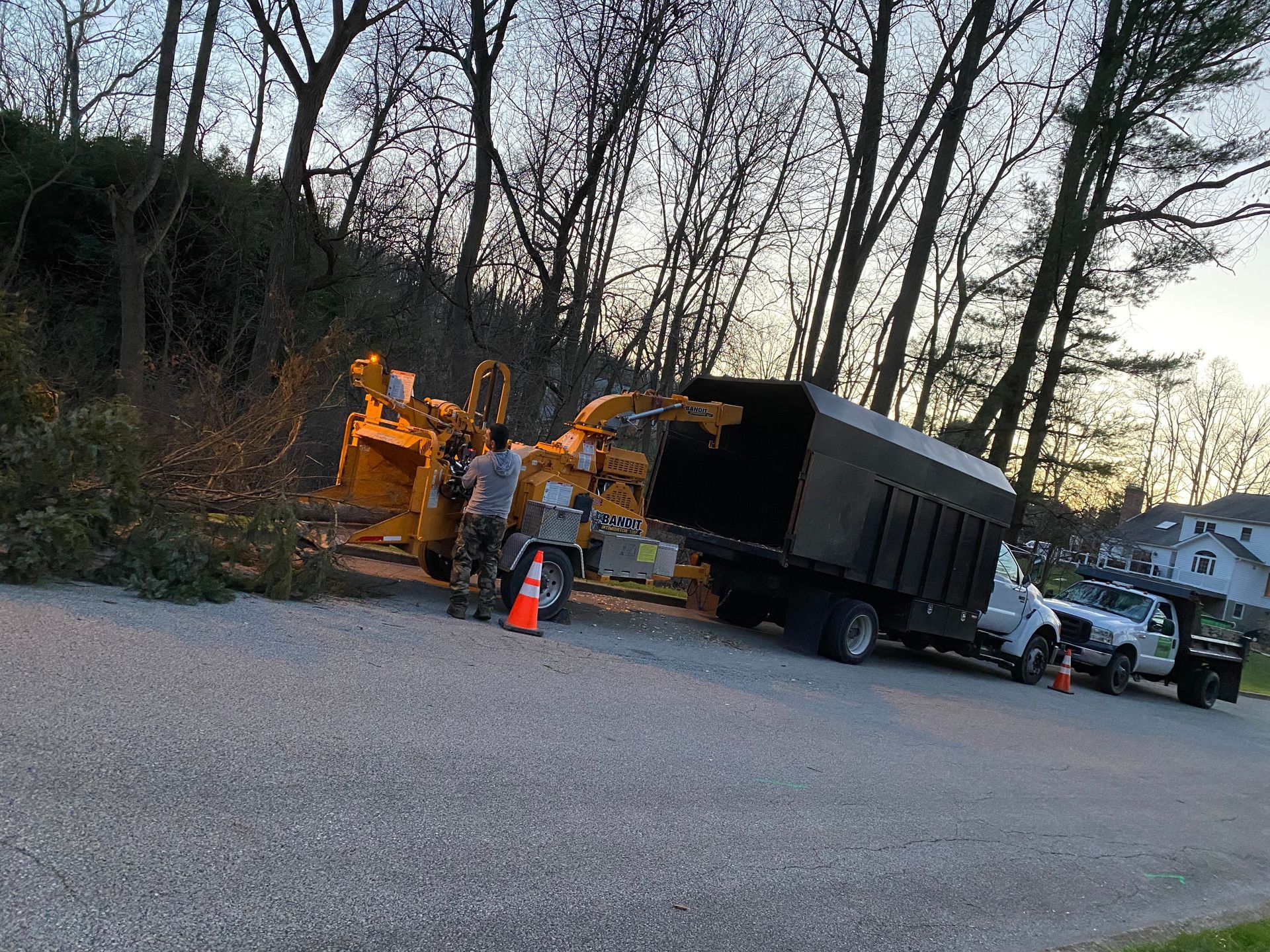 Tree service crew working on a road, using a wood chipper and truck to process branches.