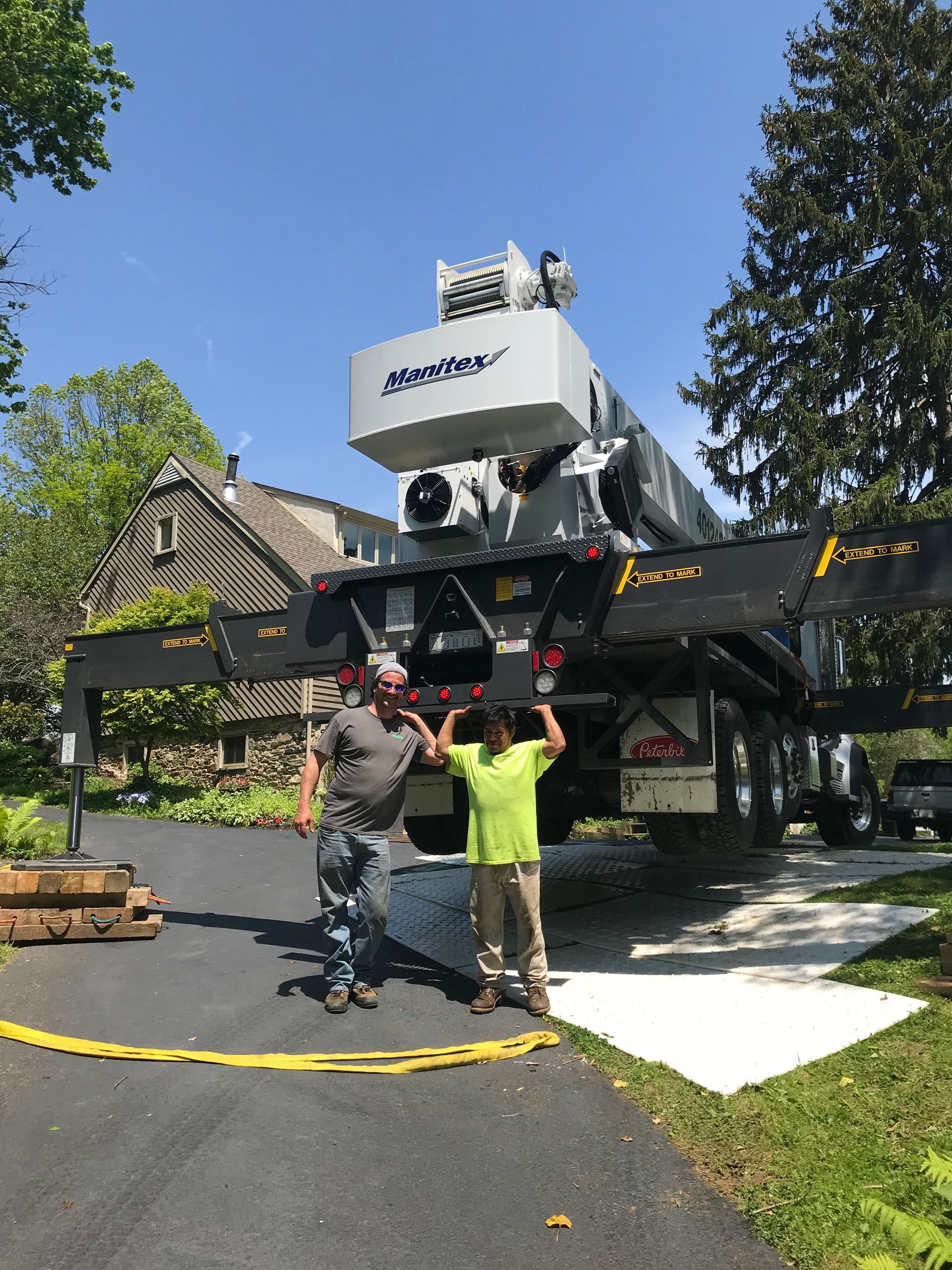 Two men stand near a large crane. Crane is parked in a driveway. Men appear to be celebrating.