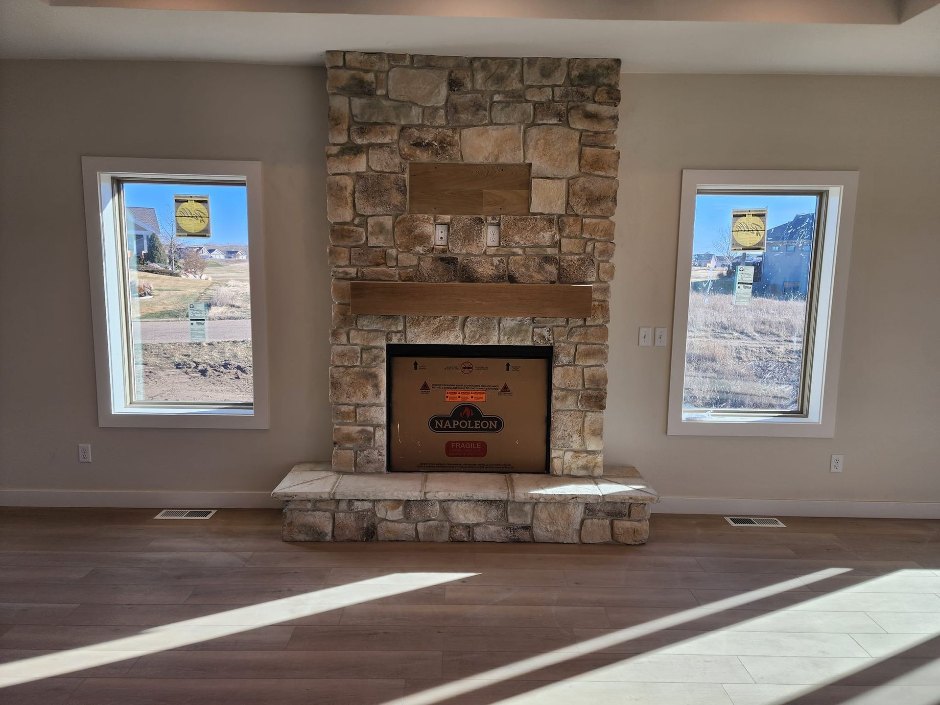 an empty living room with a stone fireplace and two windows