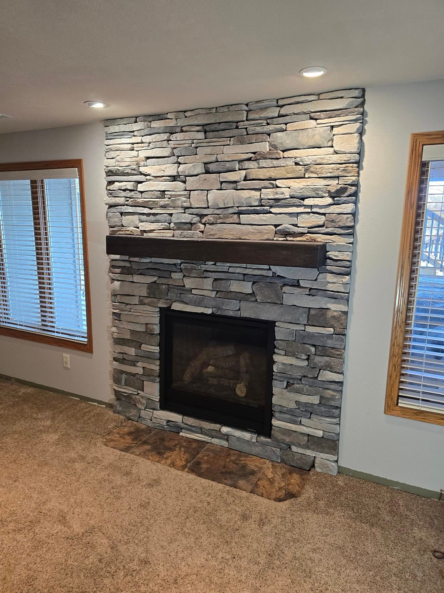 a living room with a stone fireplace and two windows