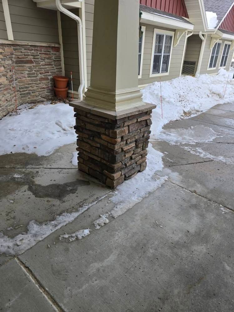 a brick column is sitting on the sidewalk in front of a house