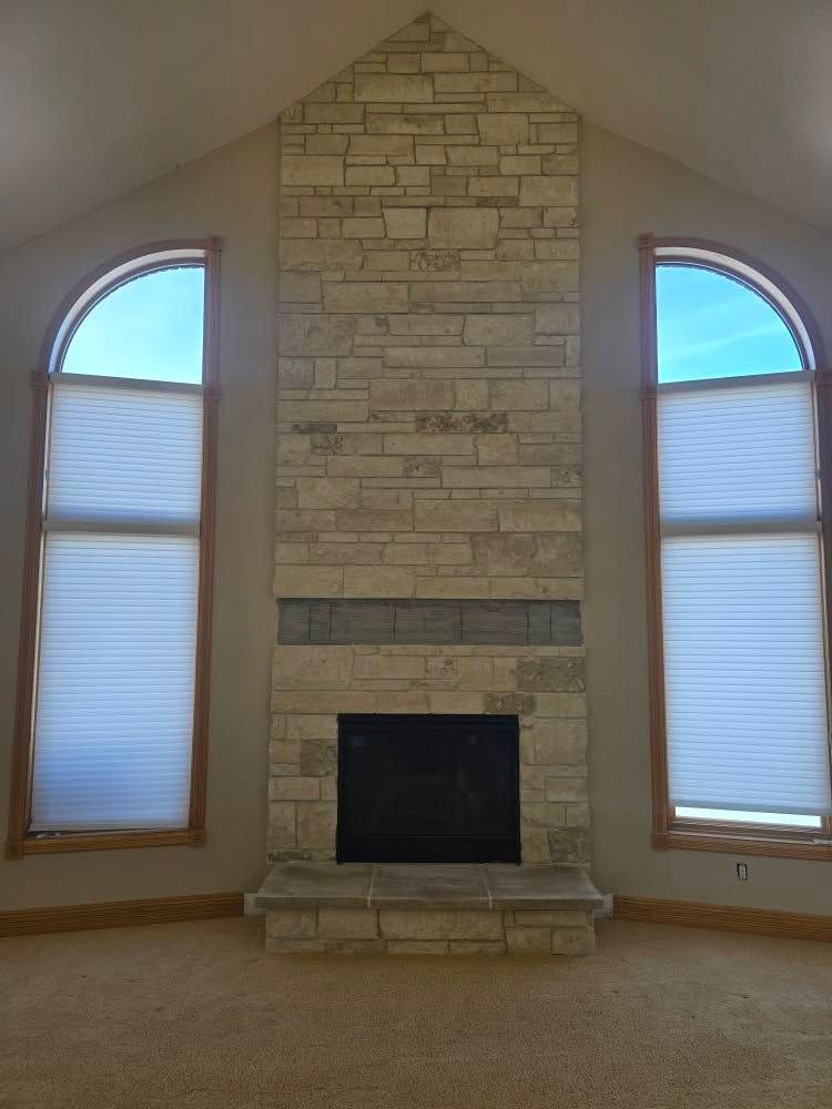 a living room with a stone fireplace and two arched windows