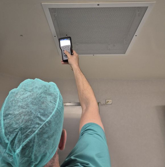 Person in teal scrubs photographing a ceiling vent with a smartphone during an inspection