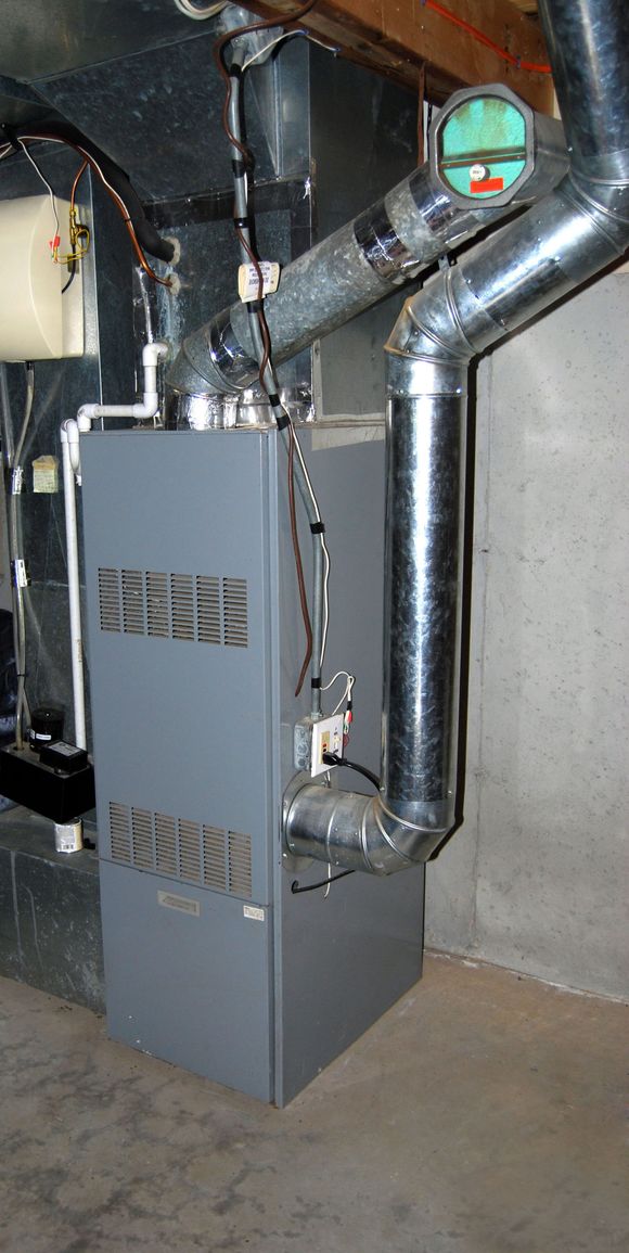 Gray furnace with metal ductwork and pipes in a basement utility area