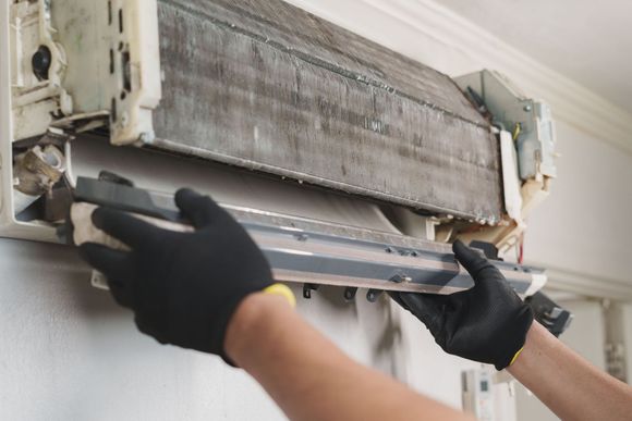 Gloved hands cleaning the filter of a wall-mounted air conditioner indoors