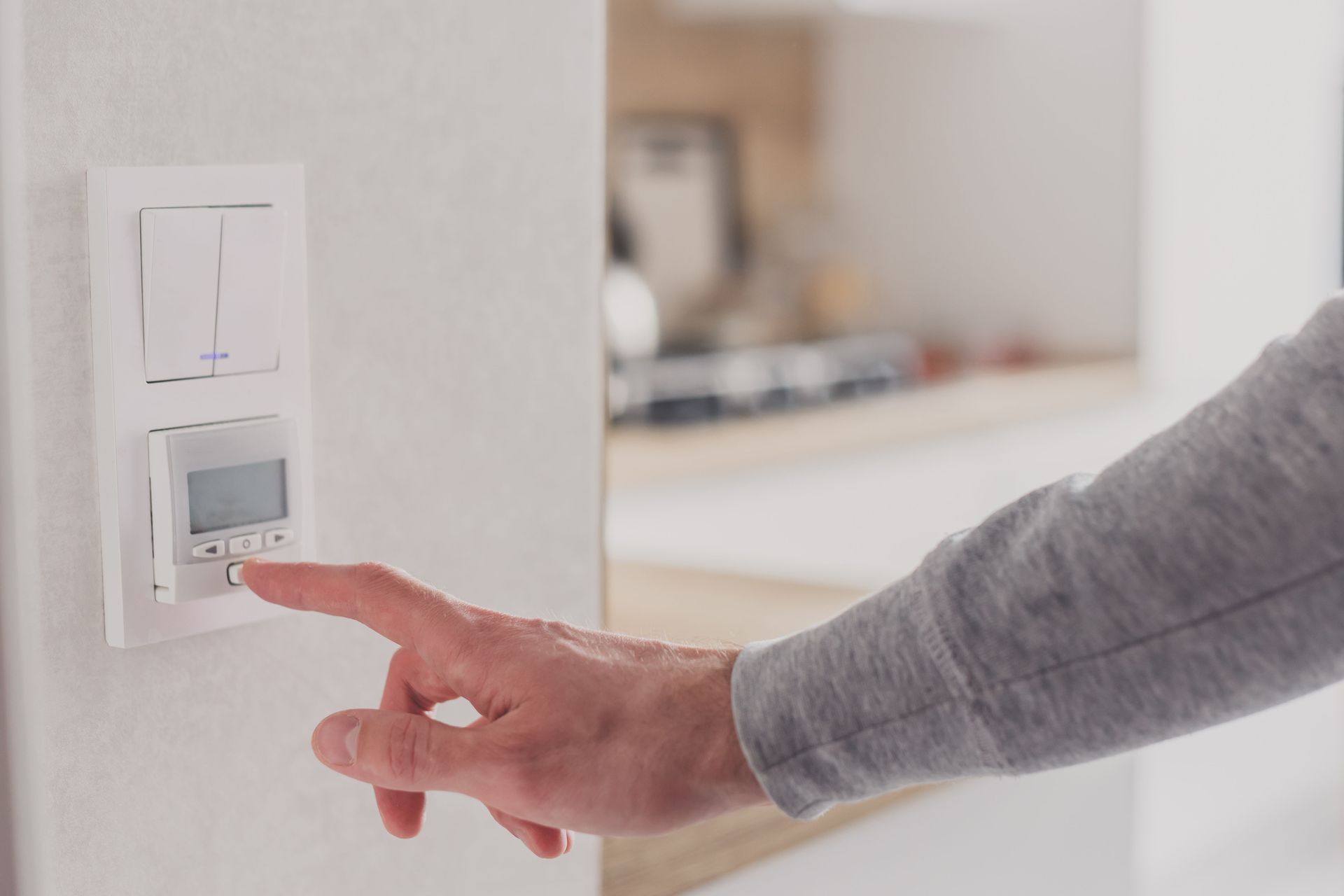 Hand pressing a wall thermostat in a bright room