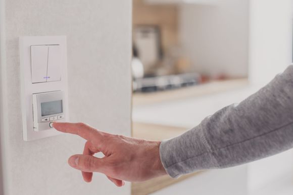 Hand pressing a wall thermostat in a bright room
