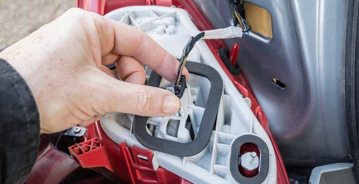 Hand holding wire connector, next to a car tail light housing, connecting a light.