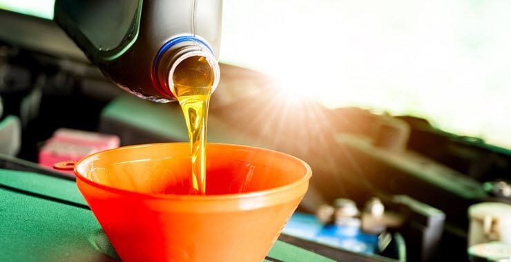 Oil being poured from a black container into an orange funnel, engine bay in background.