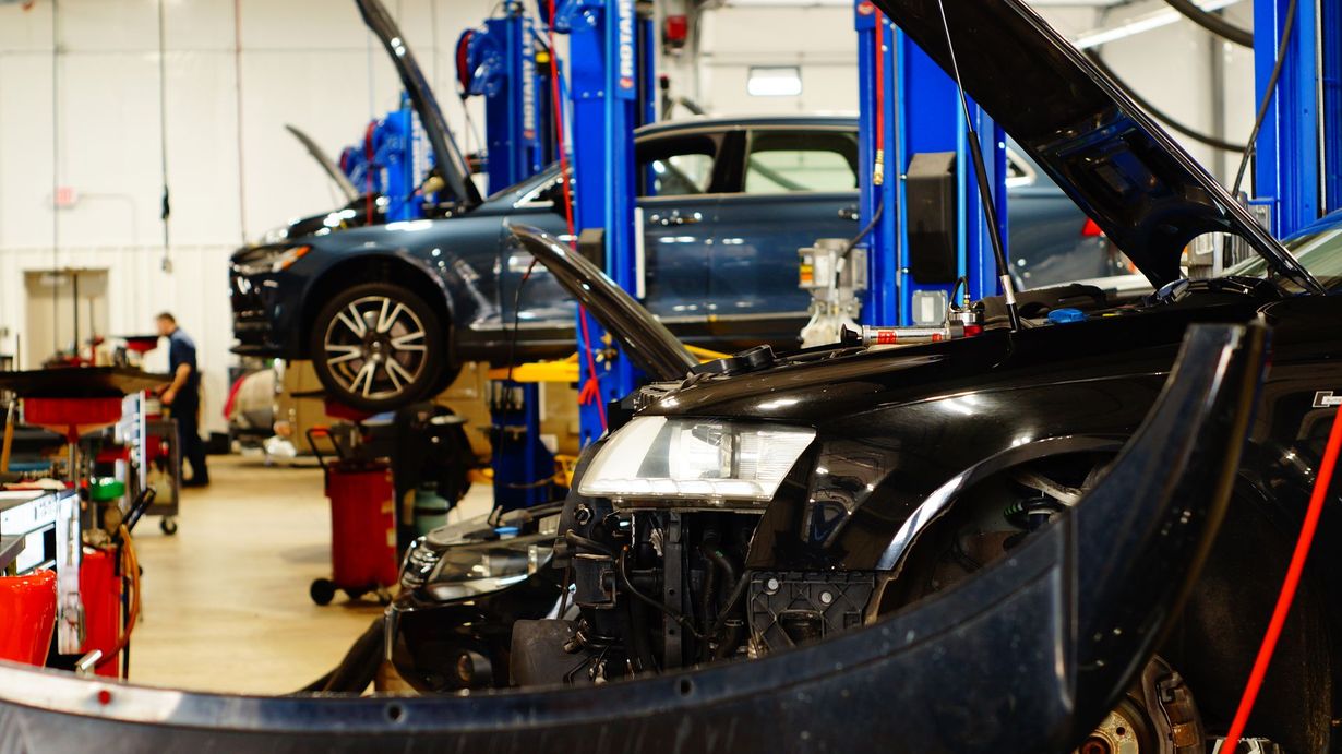 Cars on lifts in a repair shop; mechanic working. Blue and black vehicles.