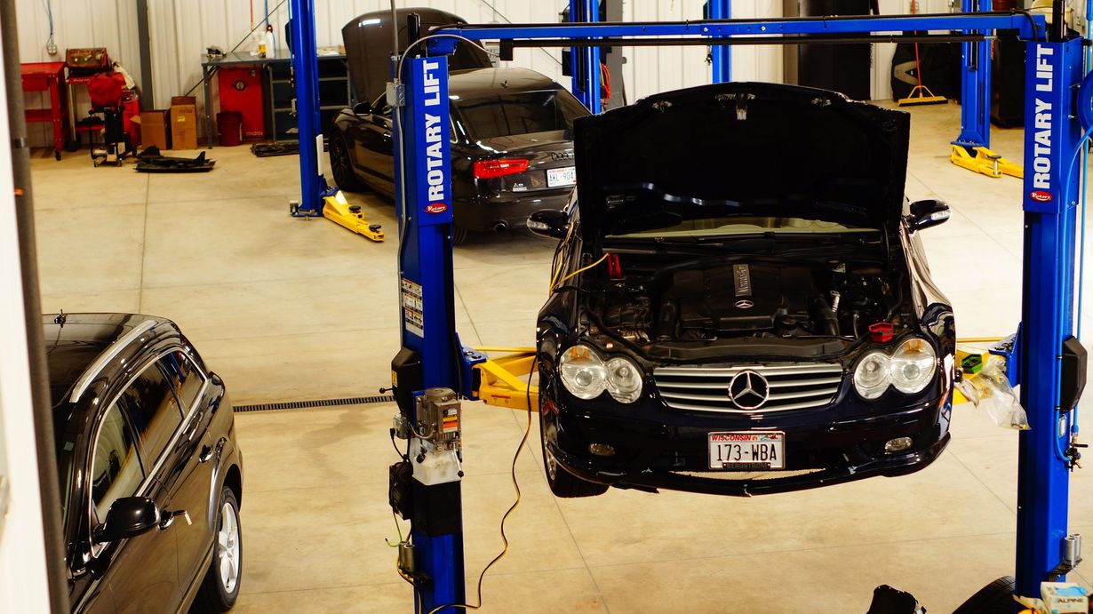 Car in auto shop being repaired, raised on lift. Another car is behind it.