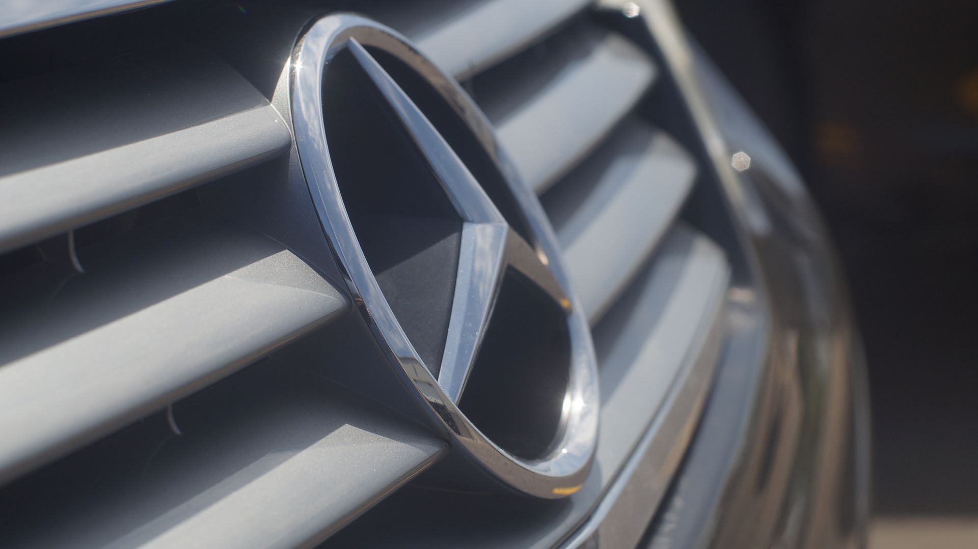 Mercedes-Benz logo on the front grill of a gray car.