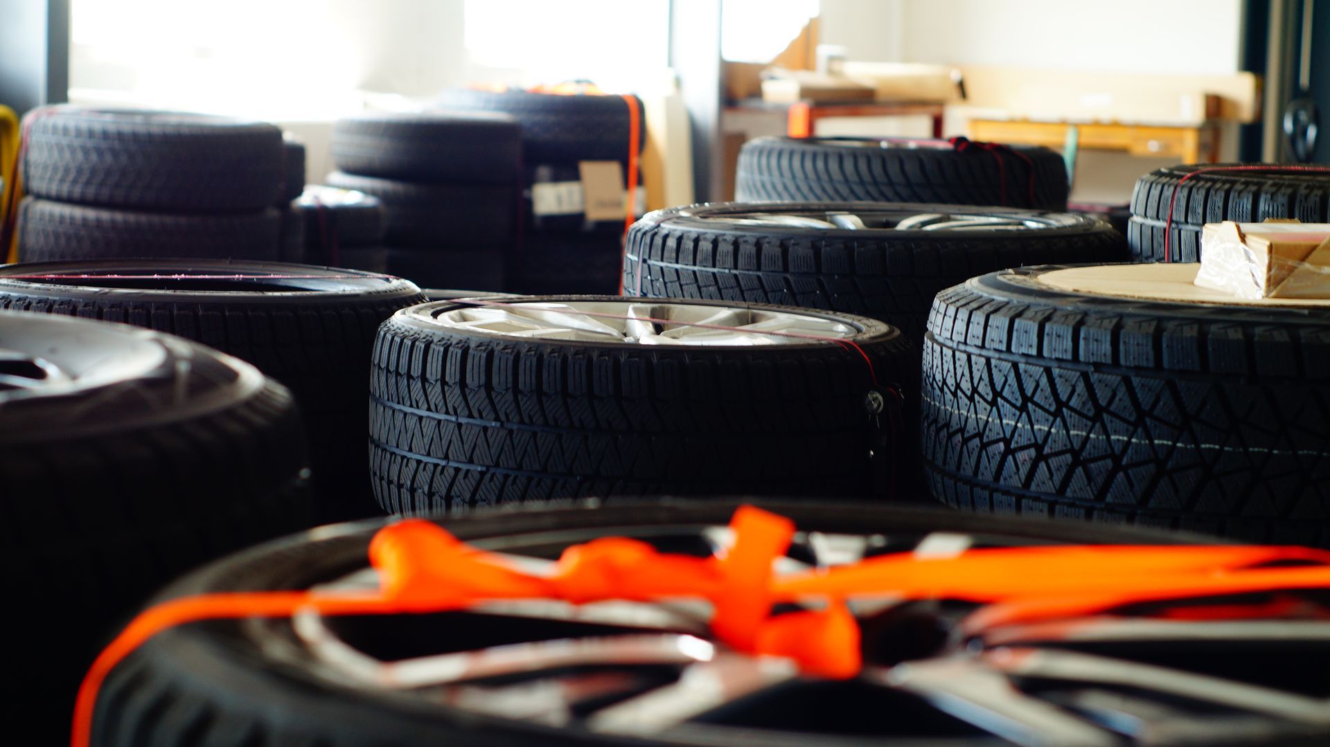 Tires stacked indoors, some with silver rims, orange straps, and black tread.