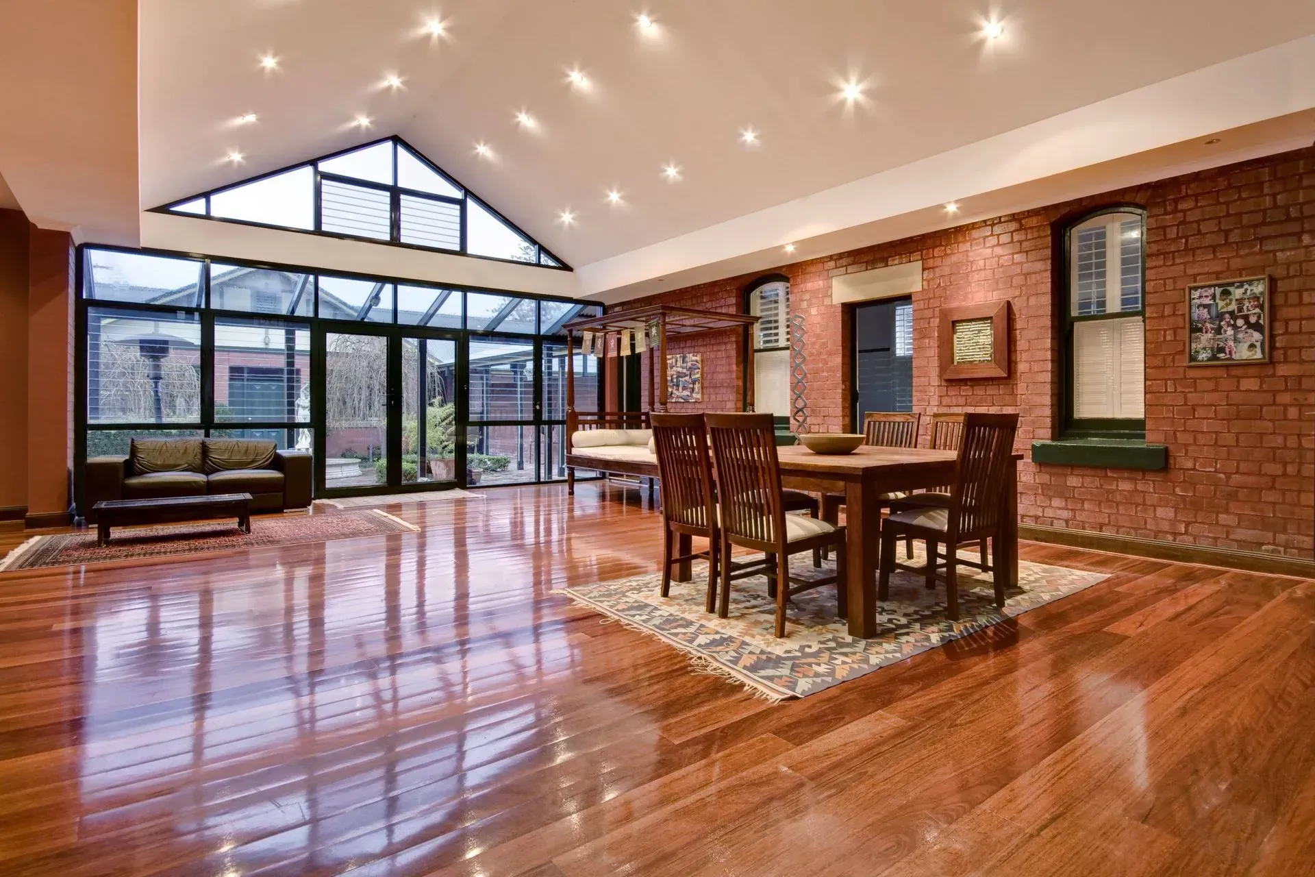 Spacious dining room with wood floor, brick wall, glass doors, and a dining table with chairs.
