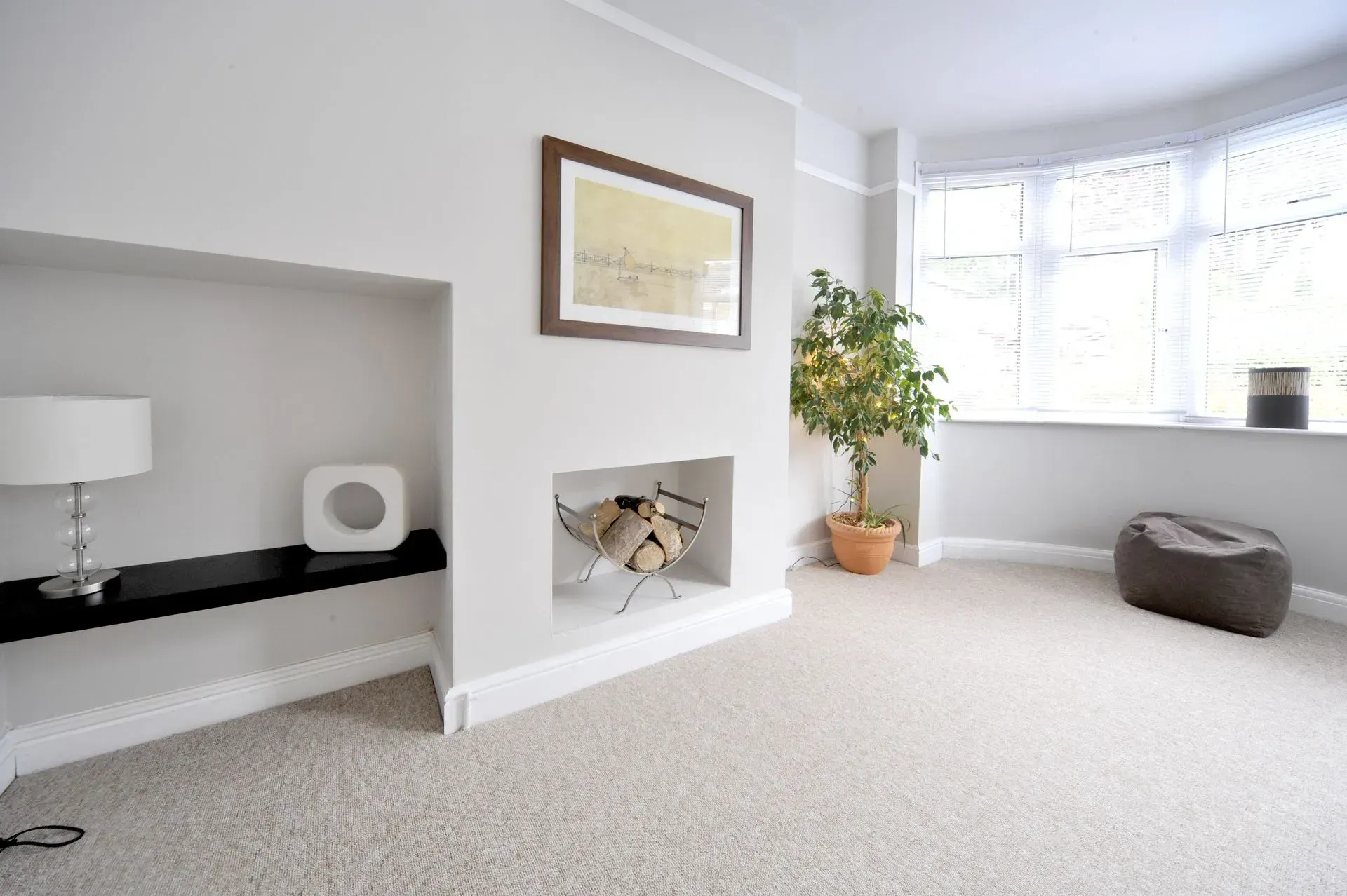 Empty living room with light gray walls, beige carpet, fireplace, and bay window.