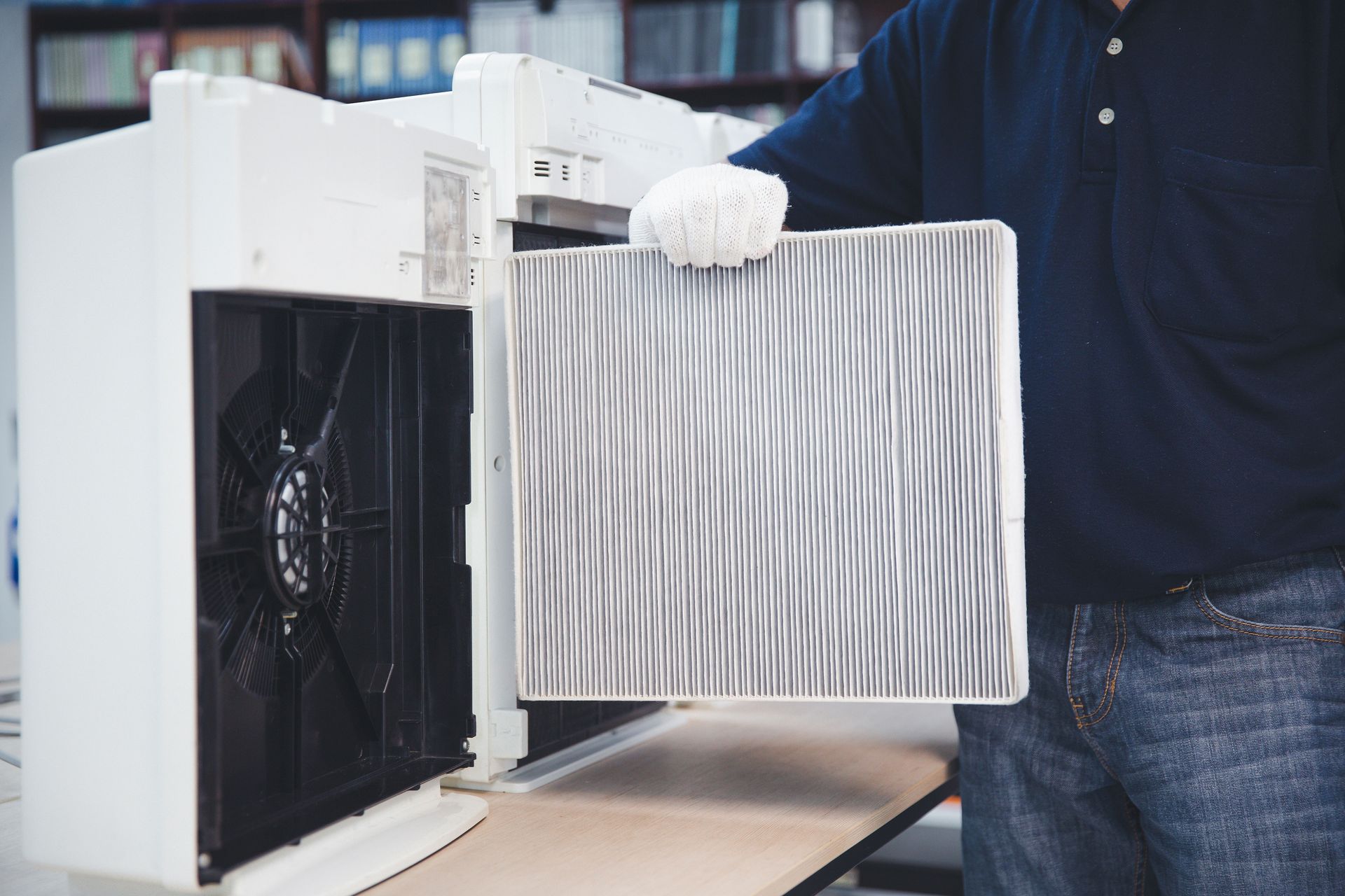 Person holding a dirty air filter beside an open HVAC unit and fan.