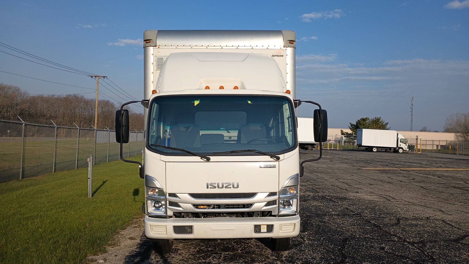 White Isuzu box truck parked on a gravel lot under a clear blue sky.
