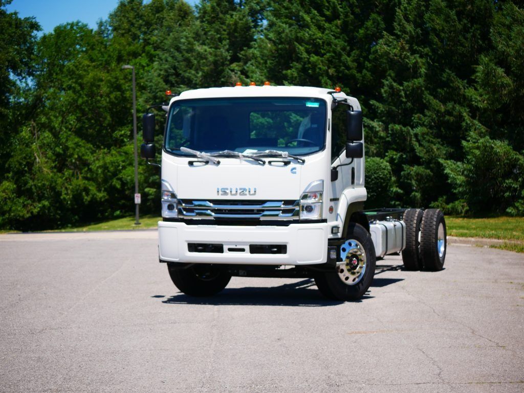 White Isuzu cab-chassis truck parked on pavement, trees in the background.