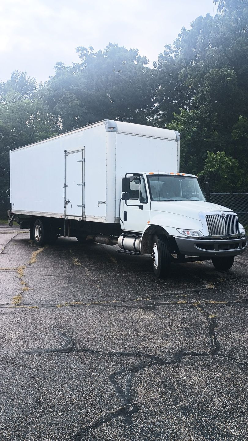 White box truck parked on asphalt, trees in background. Overcast sky.