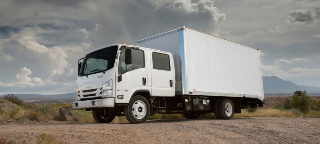 White box truck on a dirt road under a cloudy sky.