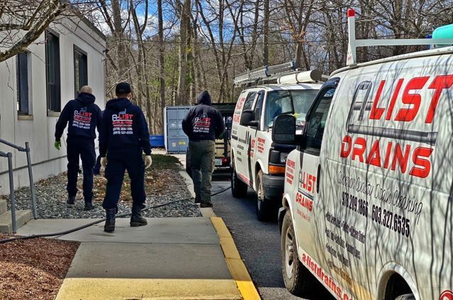 Three workers in dark uniforms walk away from a building.