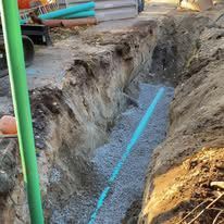 A blue pipe is being installed in a trench.