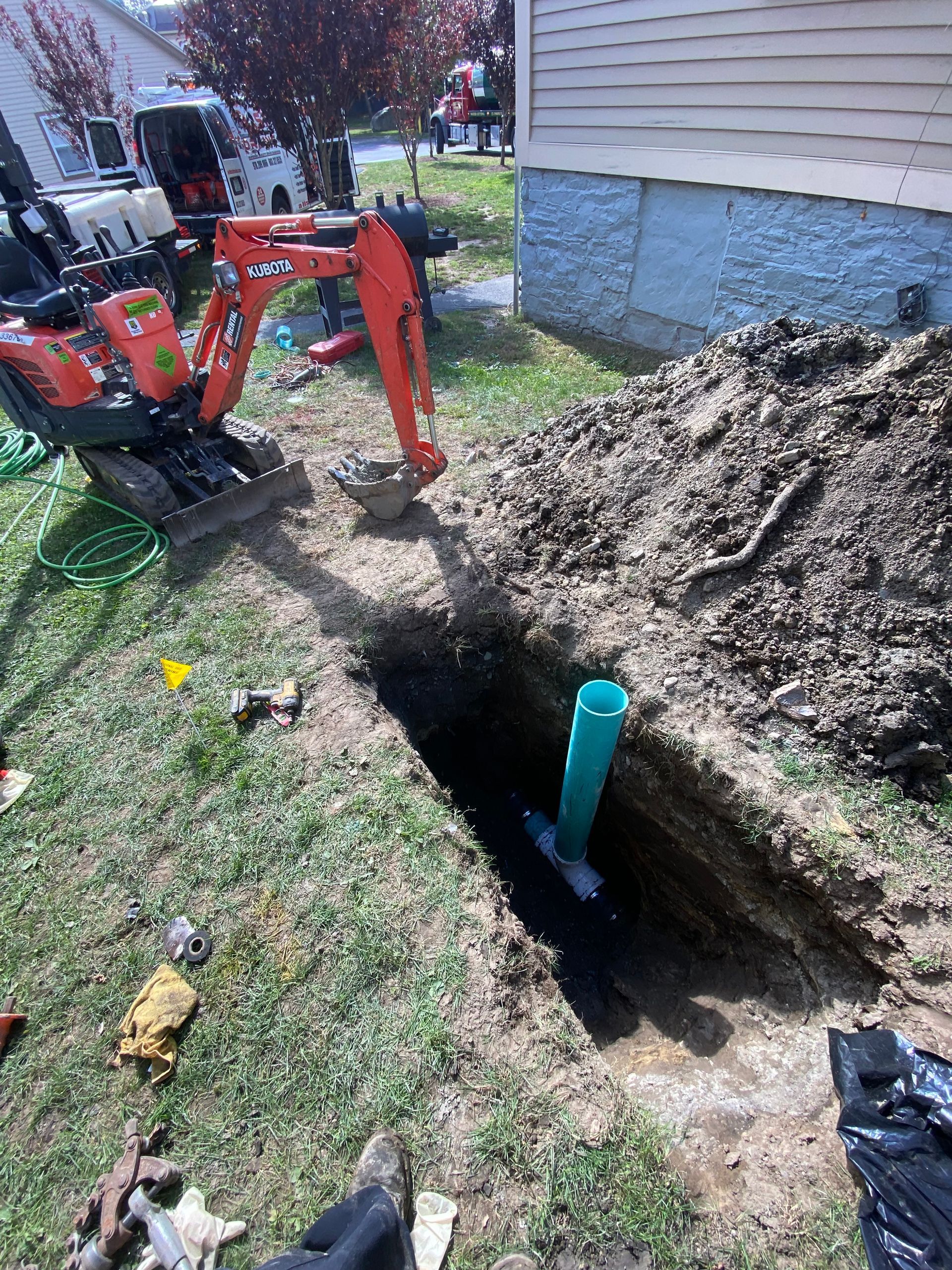 A small excavator is digging a hole in the ground in front of a house.