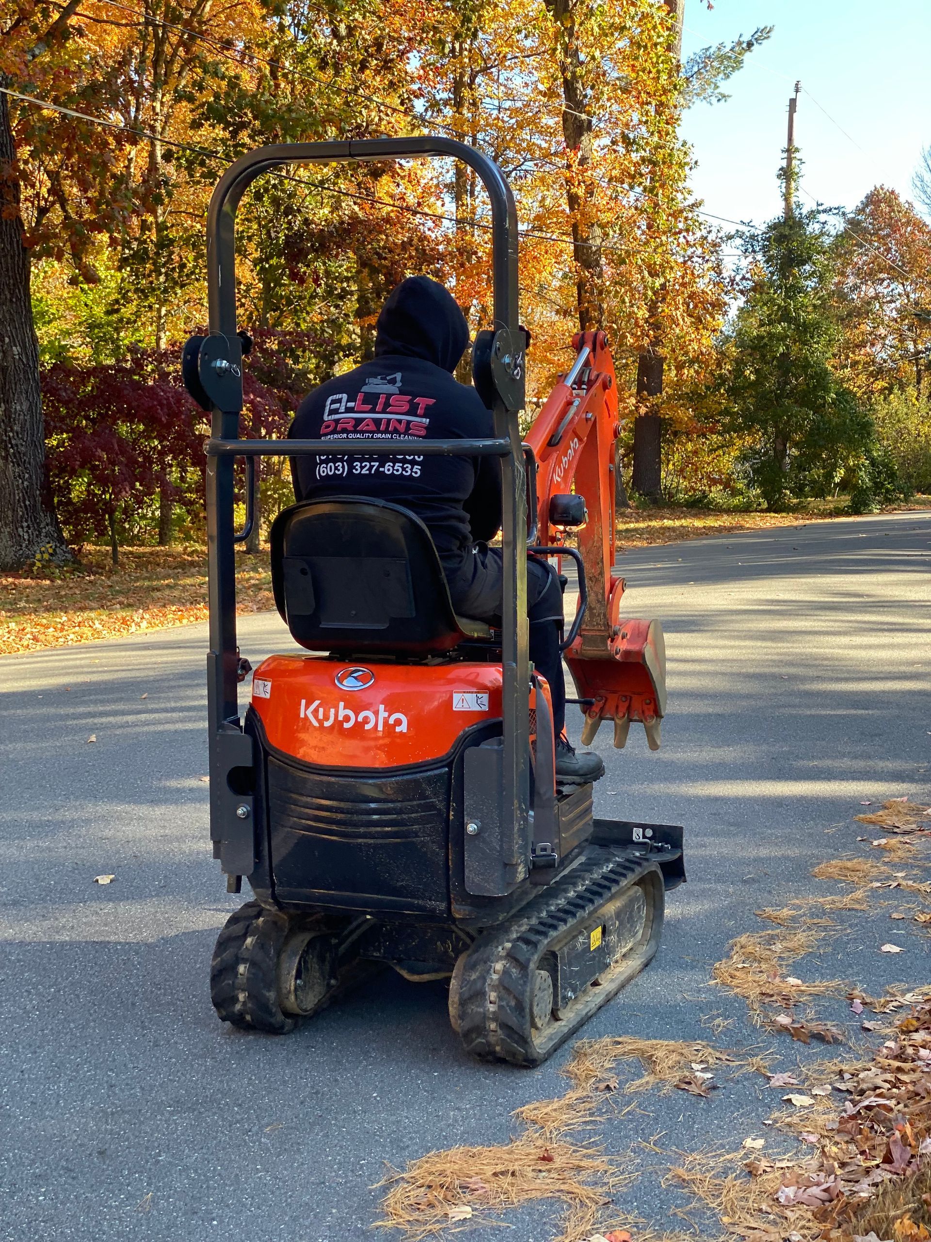 A man is driving a small orange excavator down a road.