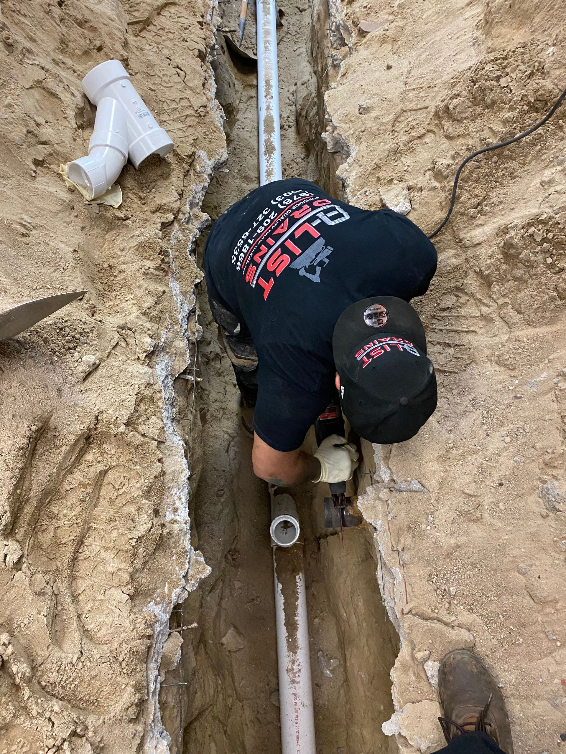 A man is working on a pipe in the dirt.