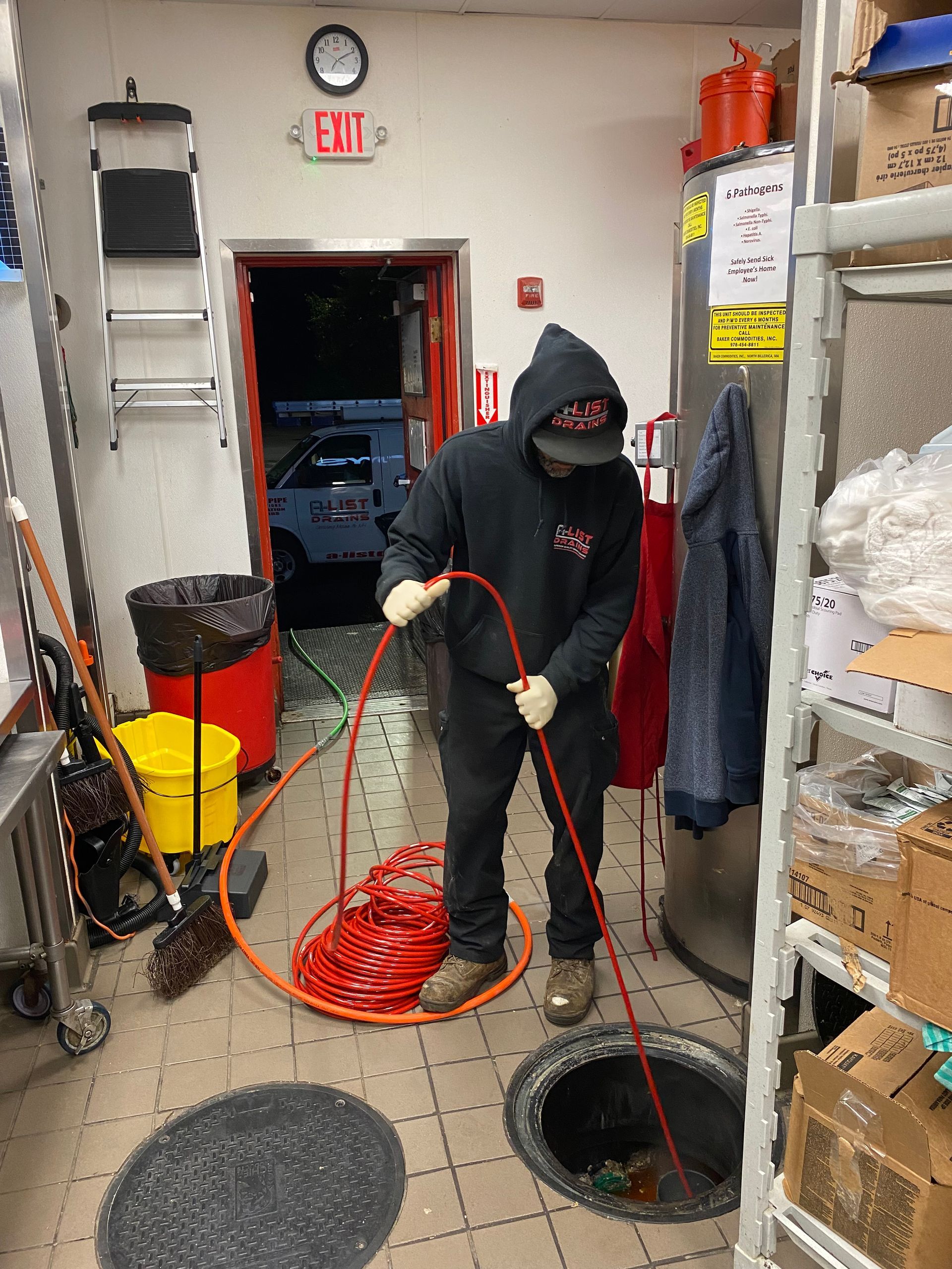 A man is working on a drain in a room with an exit sign on the wall.