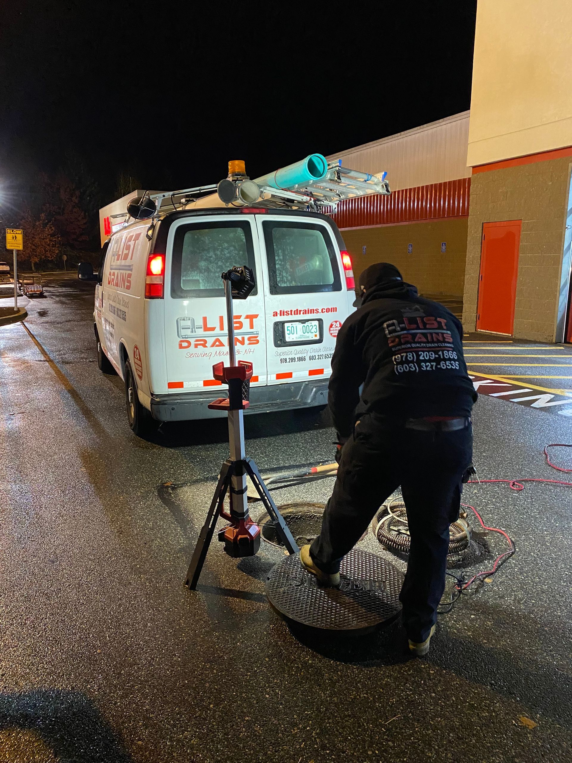 A man is working on a manhole cover in front of a van that says a-list drains