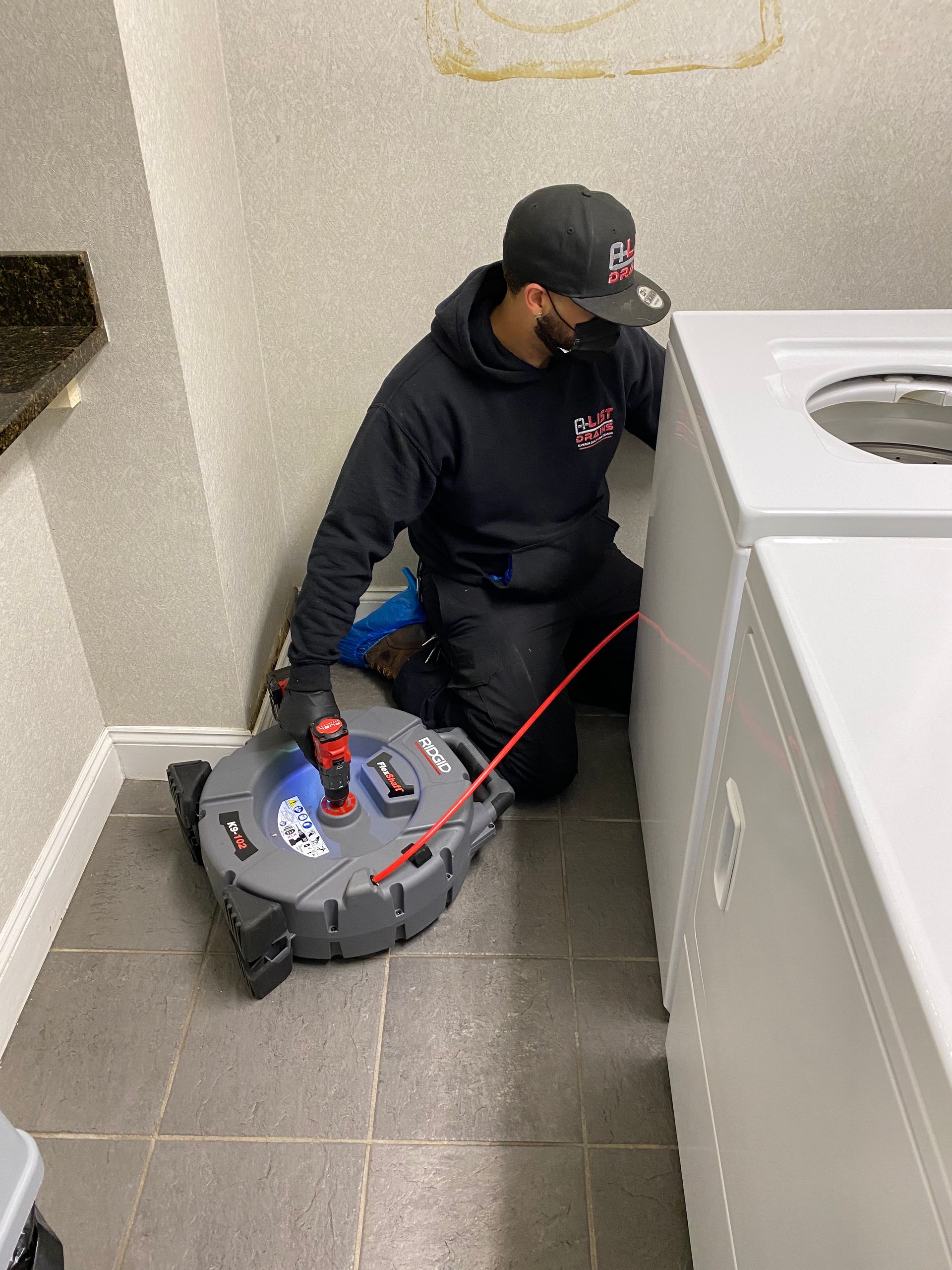 A man is kneeling down in a laundry room next to a washer and dryer.