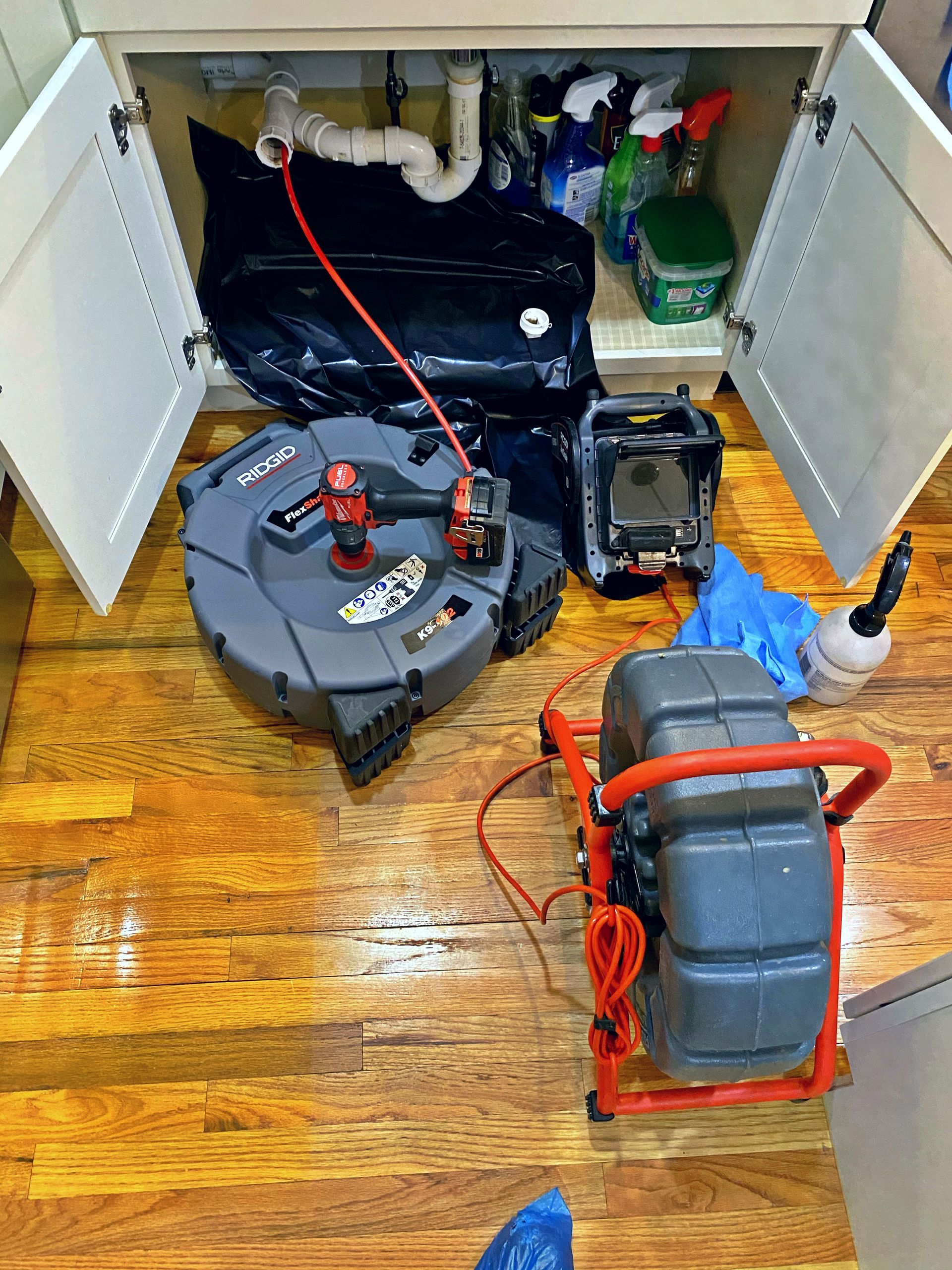 A drain cleaning machine is sitting under a sink in a kitchen.