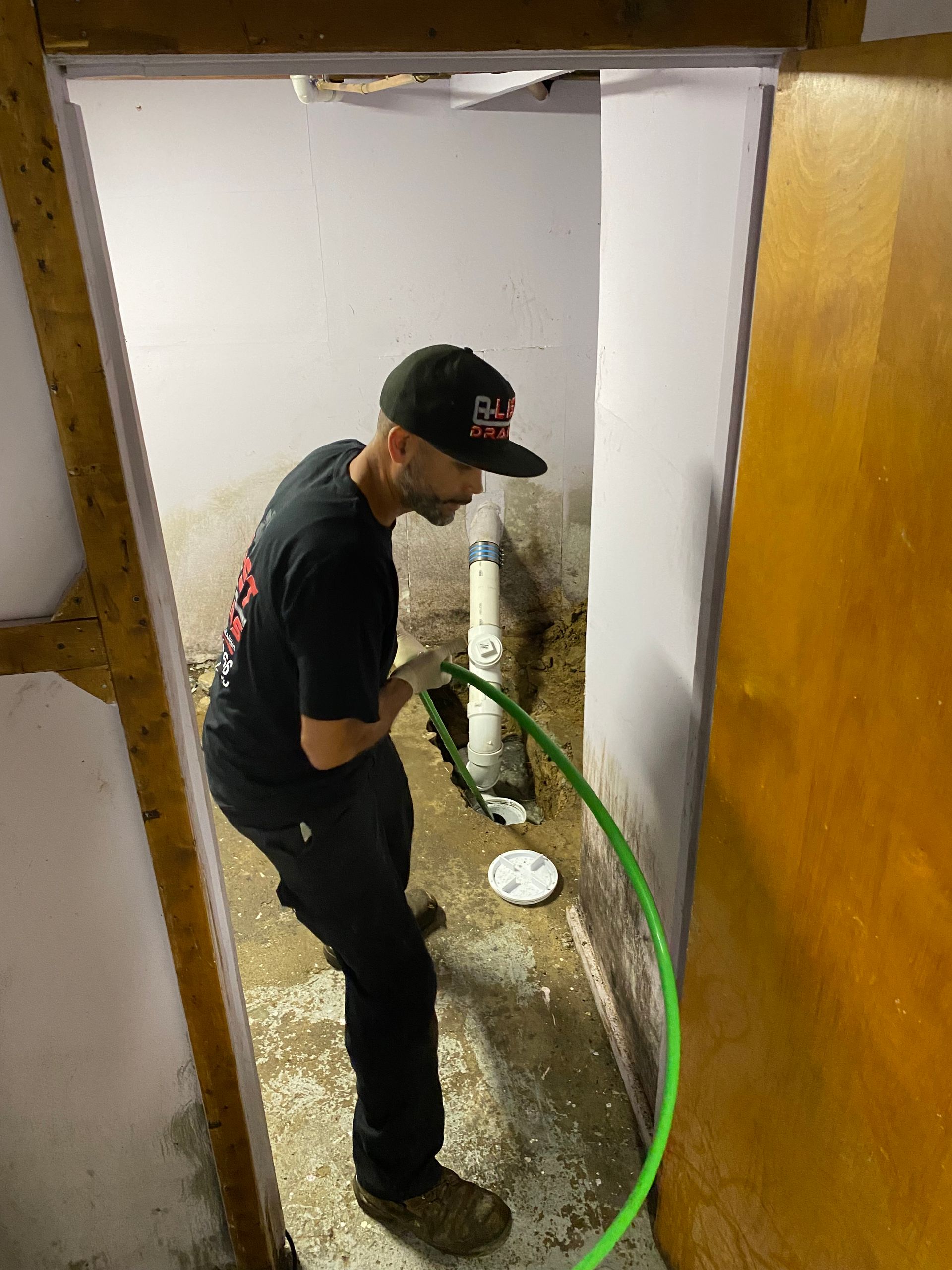 A man is working on a pipe in a basement with a green hose.