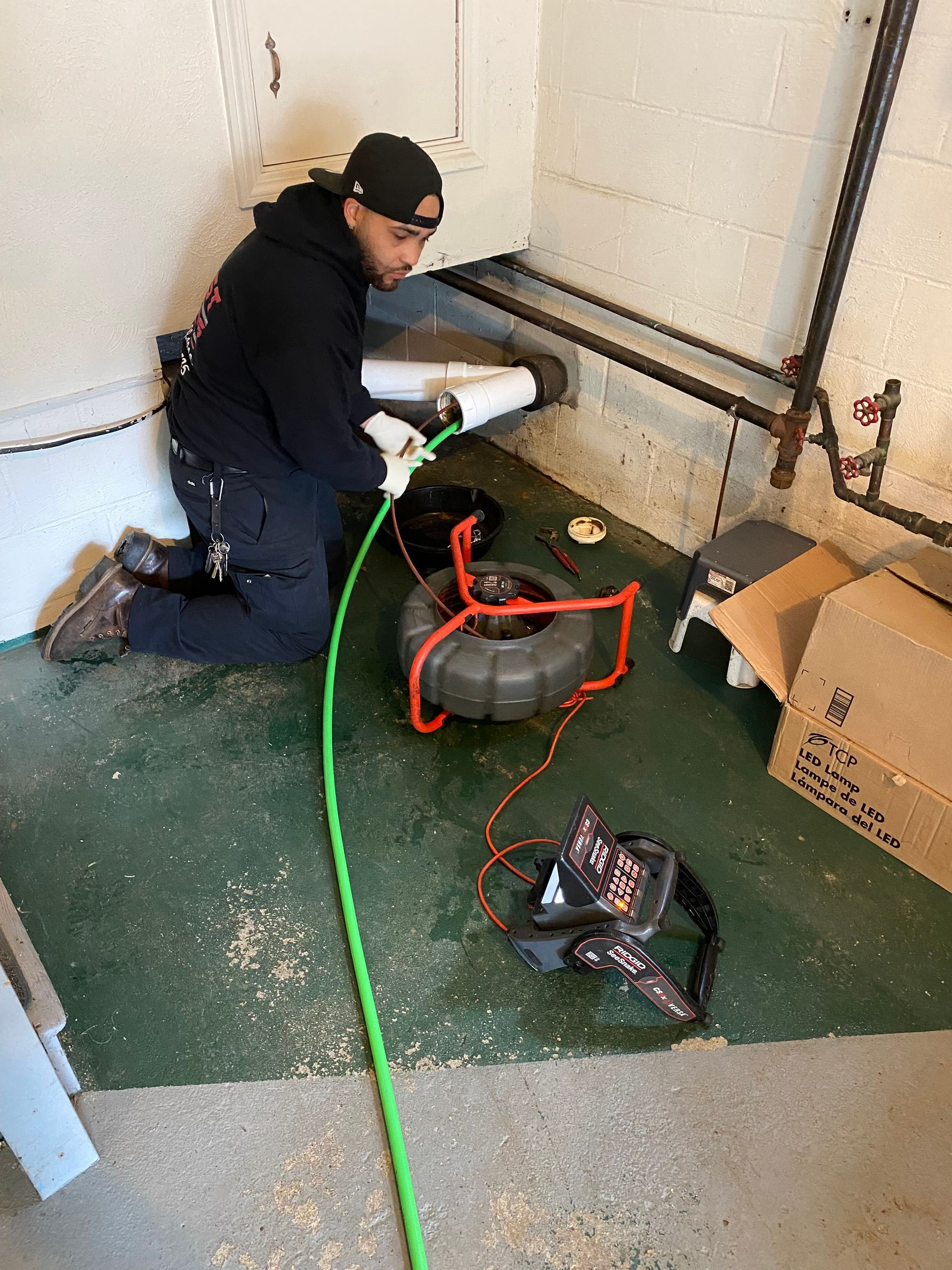 A man is kneeling down in a room with a hose and a camera.