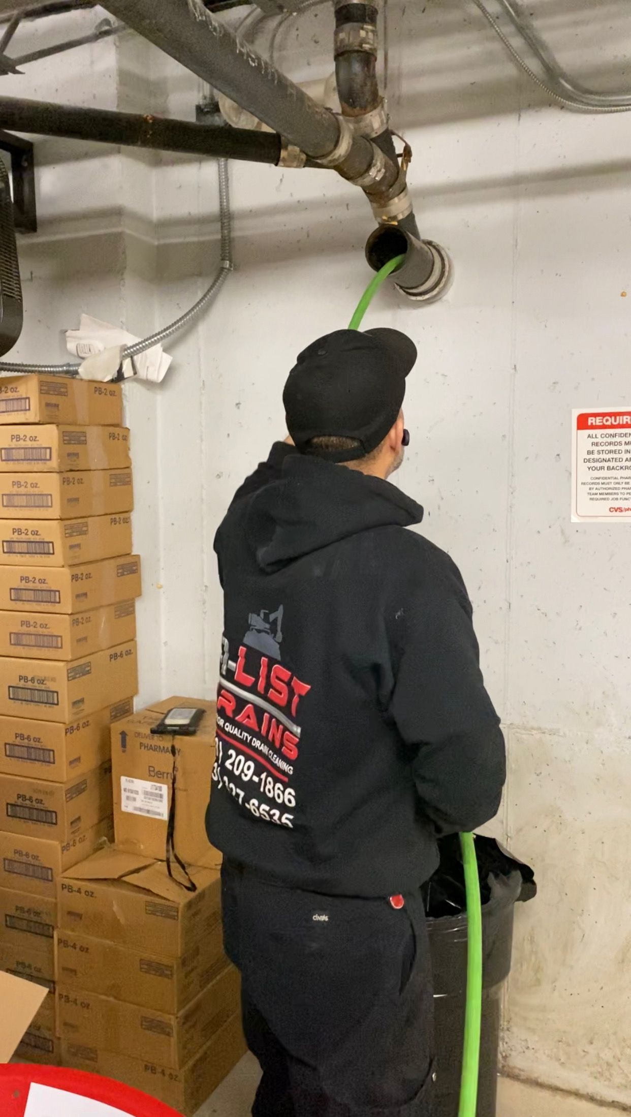 A man in a black hoodie is holding a green hose.