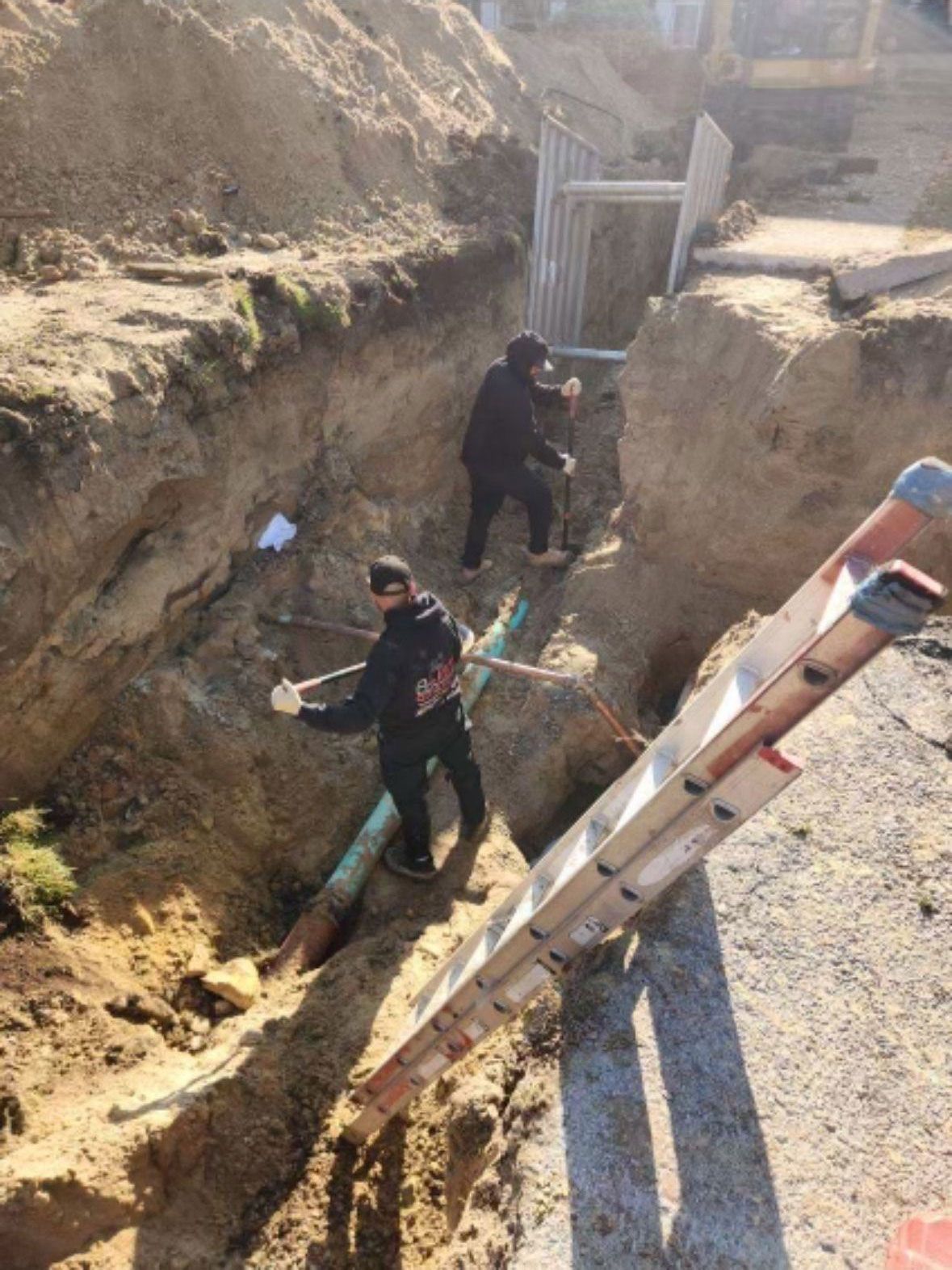 Two men are working in a trench next to a ladder.
