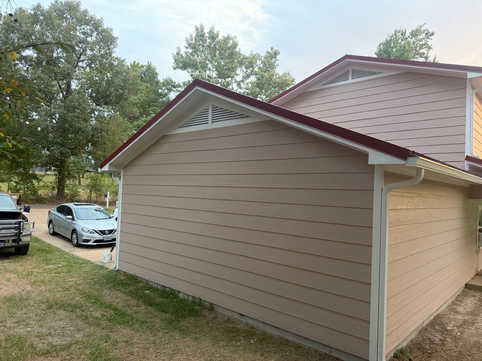 Beige detached garage with maroon trim and trees in the background