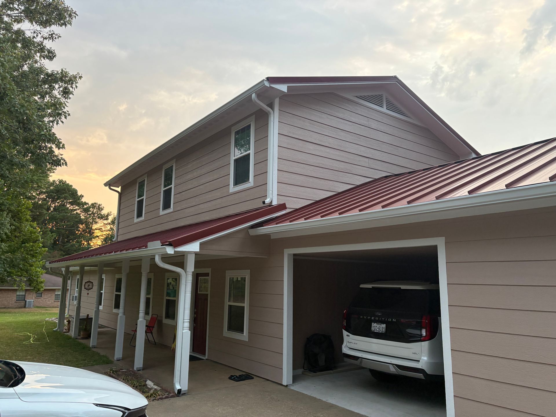 Two-story beige house with red metal roof and car parked in a covered driveway