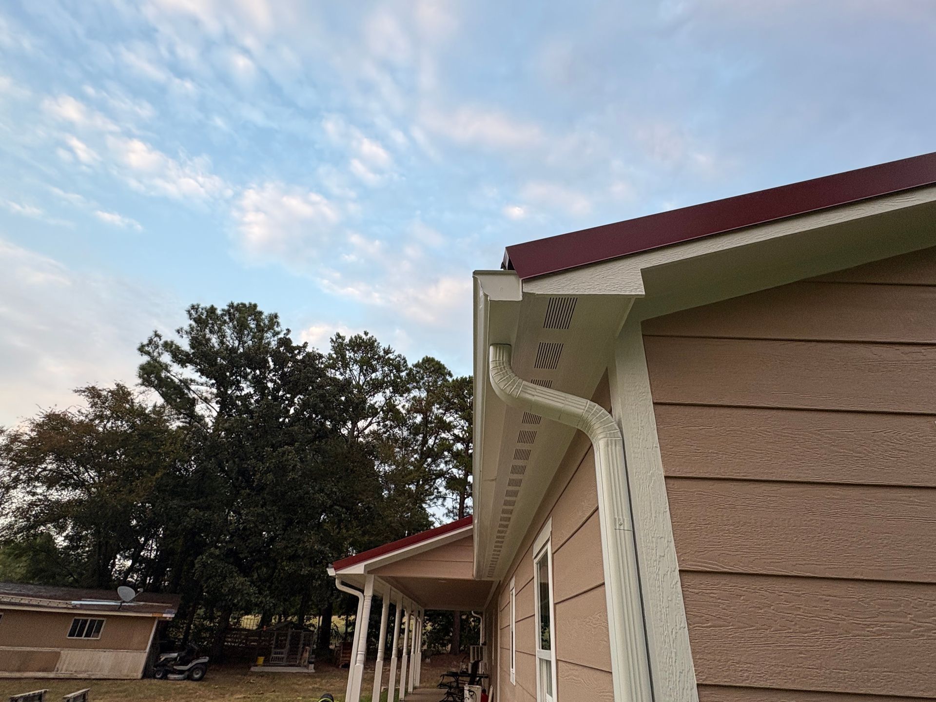 Exterior of a tan building with white eaves and red roof under a partly cloudy sky