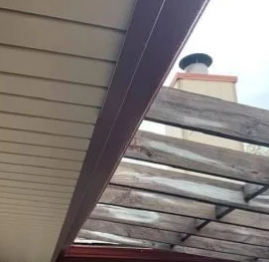 Under a slanted roof, weathered transparent panels and a chimney against the sky