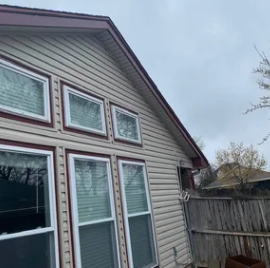 House exterior with beige siding, large windows, and a wooden fence under a cloudy sky
